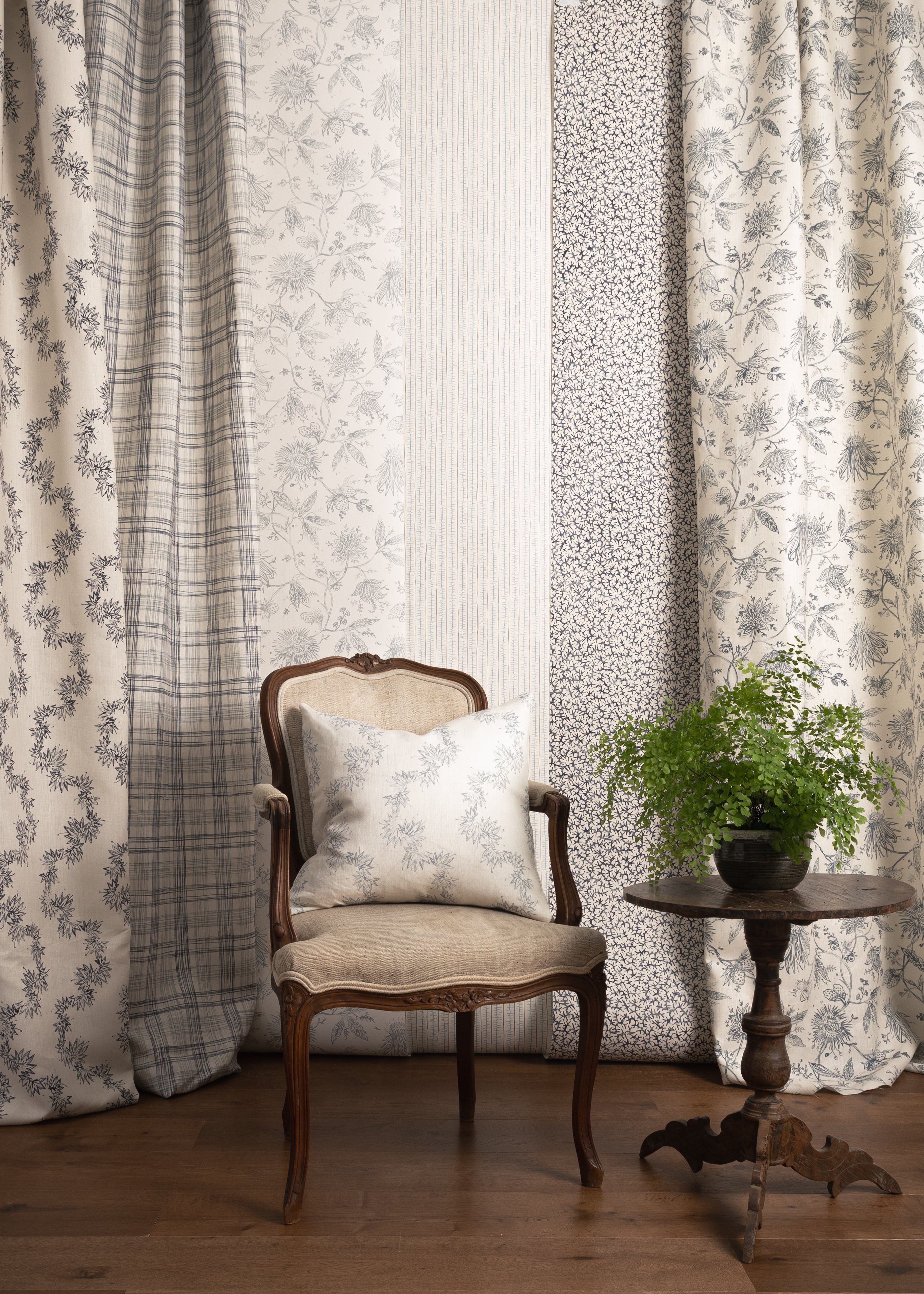 Chair with a pillow in front of panels of fabric and wallpapers in various patterns in blue colors.
