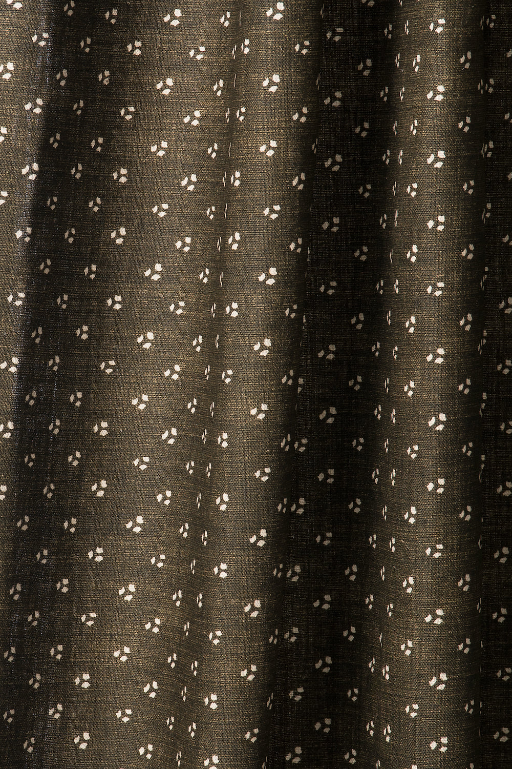 Draped printed fabric in a clustered dot pattern in cream on a dark brown field.