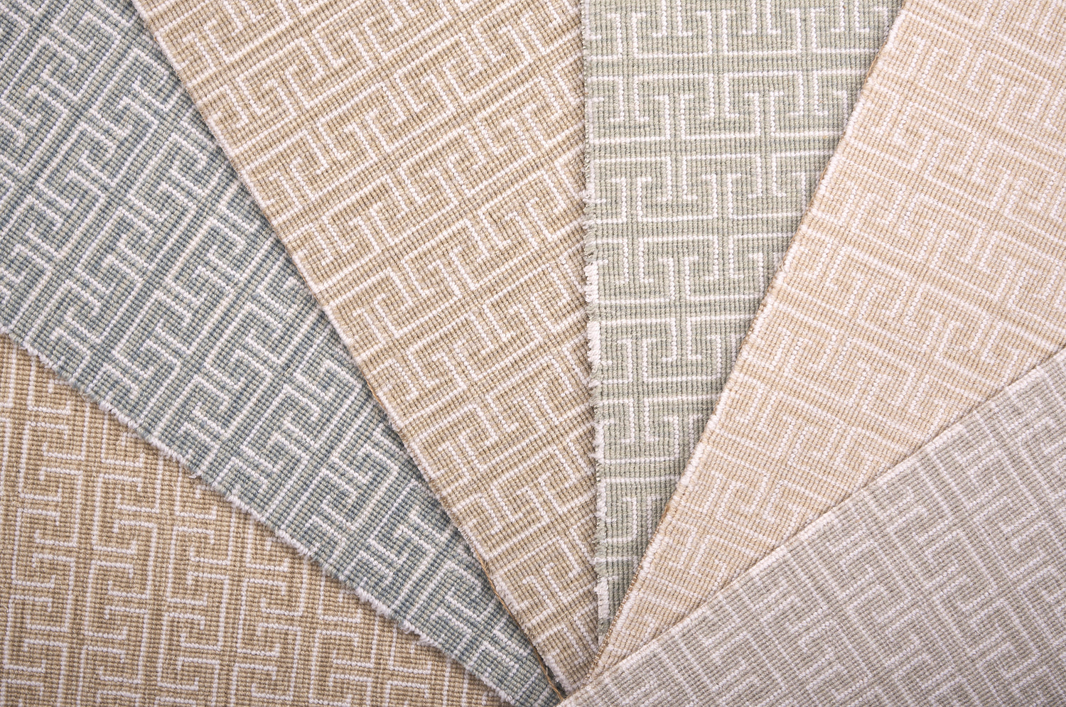 Stack of broadloom carpet samples with geometric Greek pattern in soft pastels.