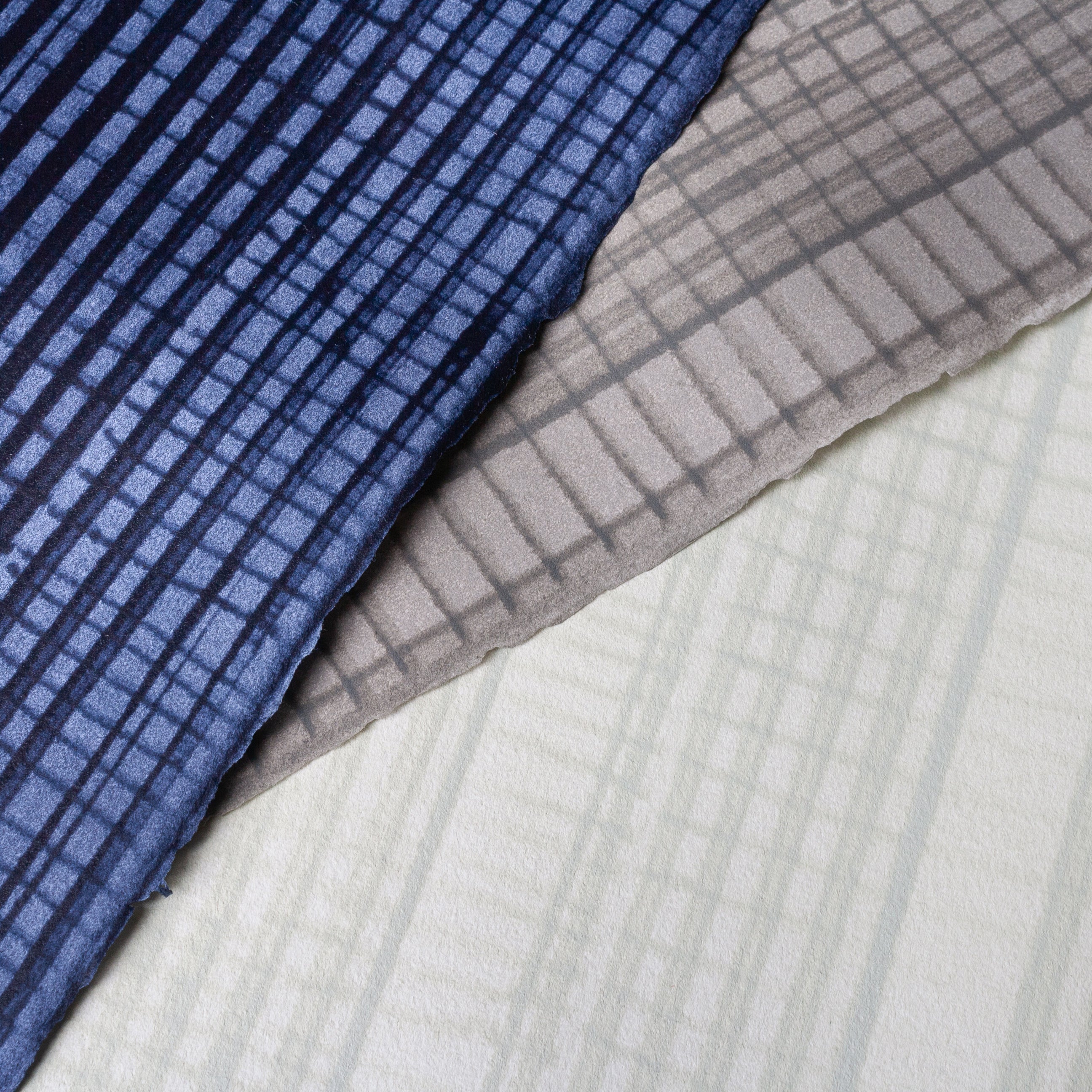 Pile of wallpaper swatches with irregular grid patterns in shades of blue, gray and cream.