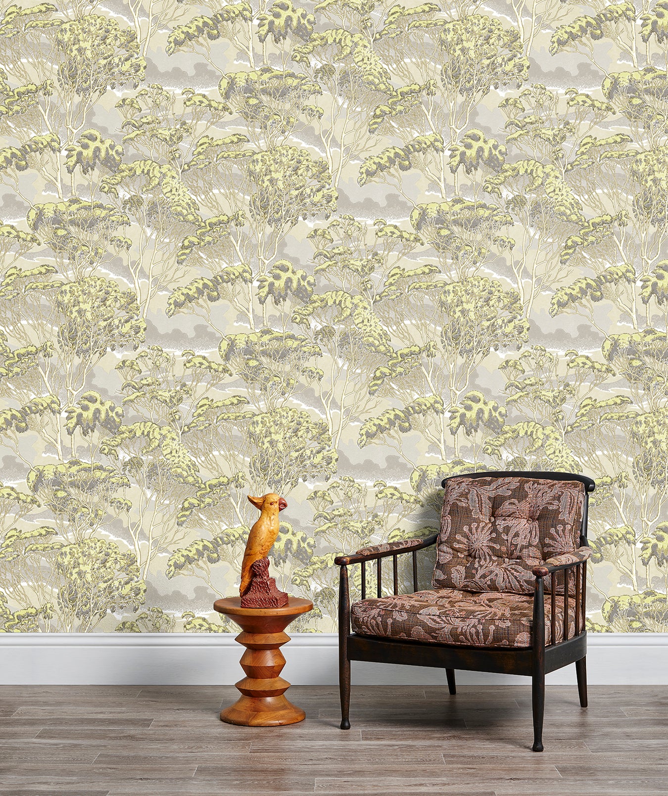 Armchair and end table in front of a wall papered in a painterly tree print in gray, yellow and cream.