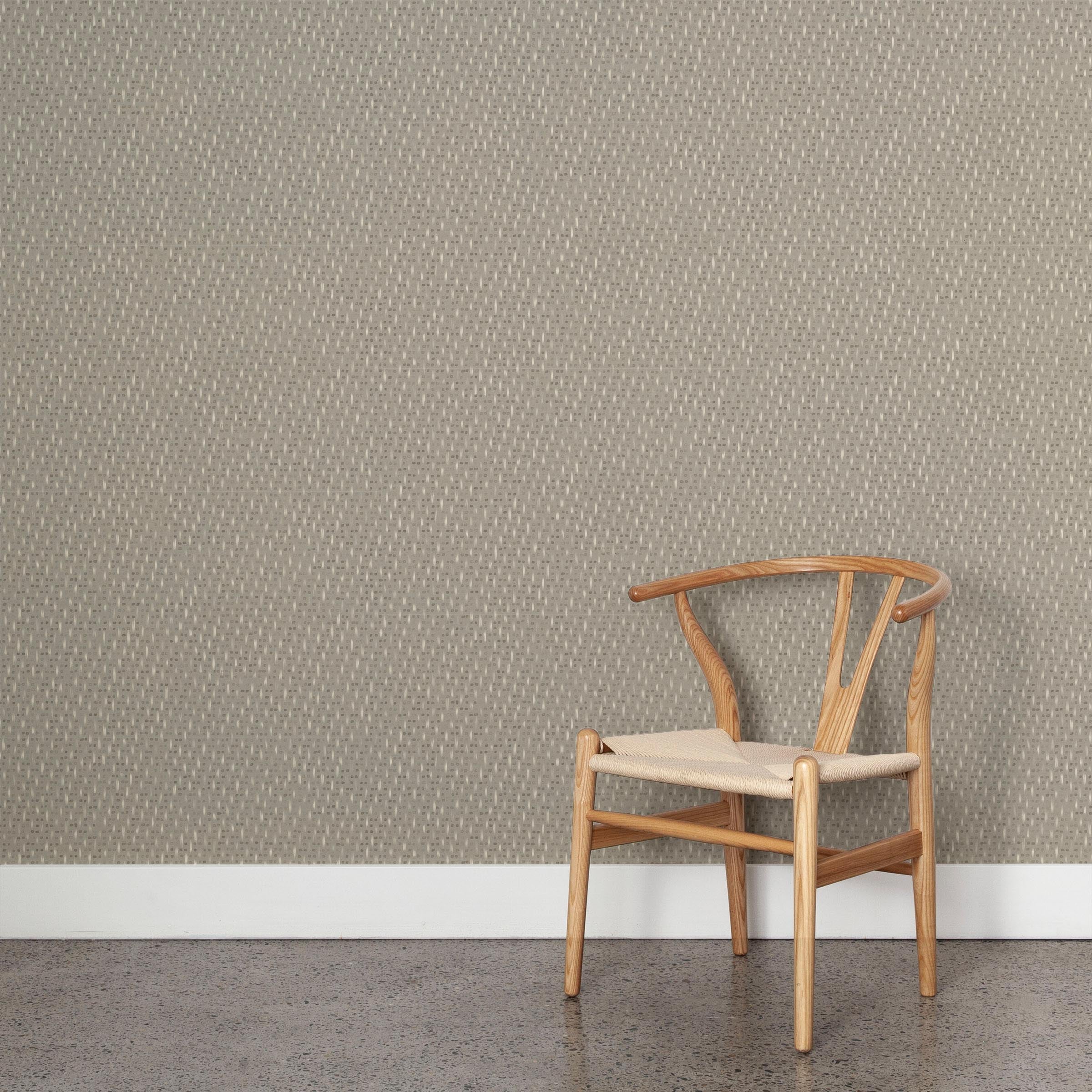 A wooden chair stands in front of a wall papered in a small-scale dot and dash pattern in cream and gray on a light gray field.