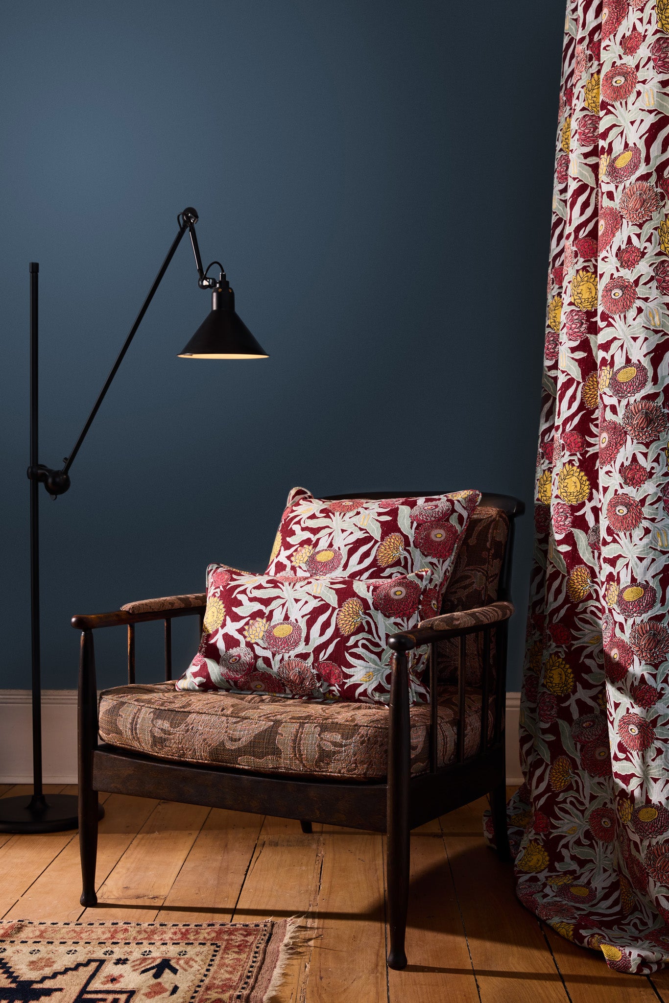 Wooden side chair with floral printed upholstery and pillows against a teal wall, with a curtain in the same floral design. 