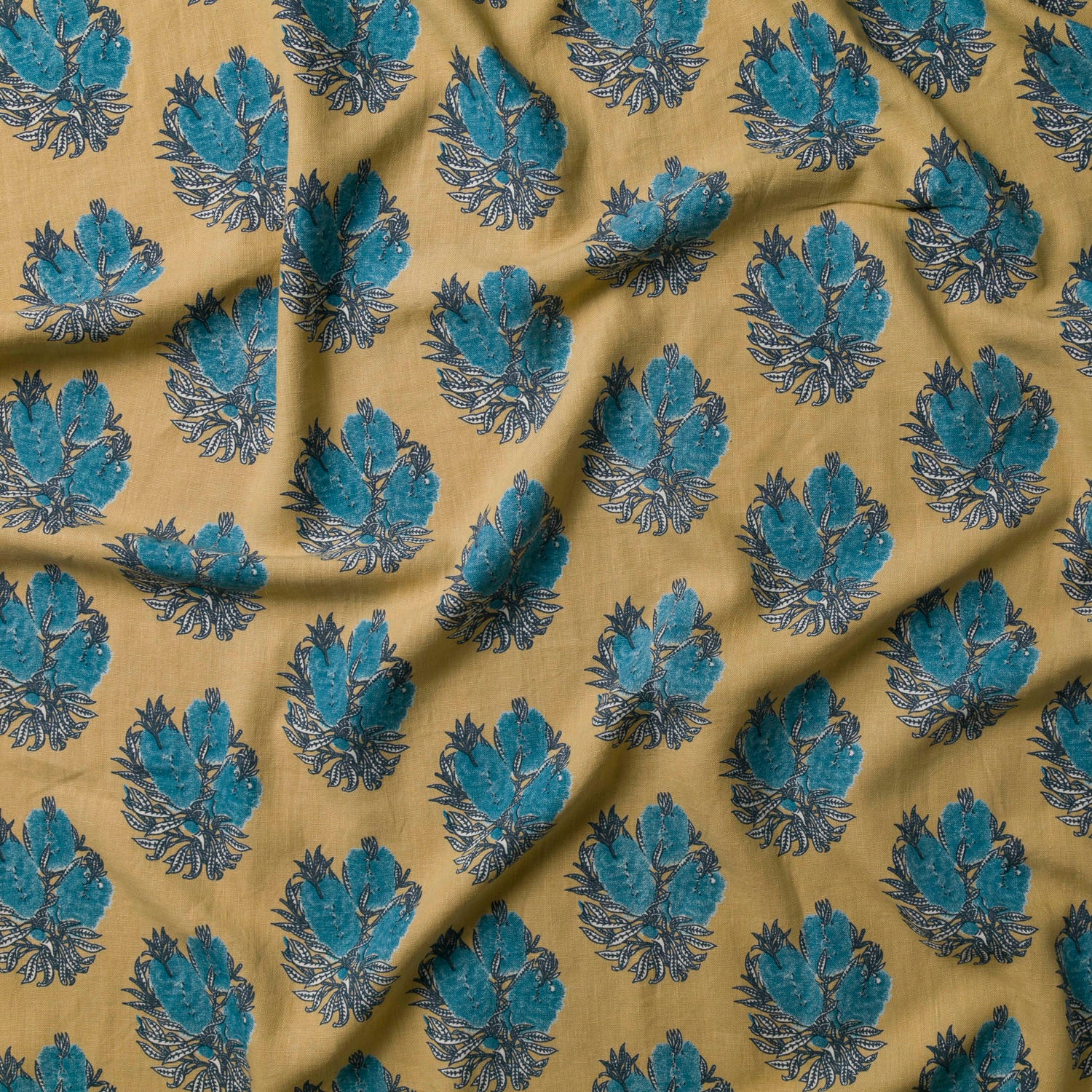 Draped fabric in a floral cameo print in blue and gray on a mustard field.
