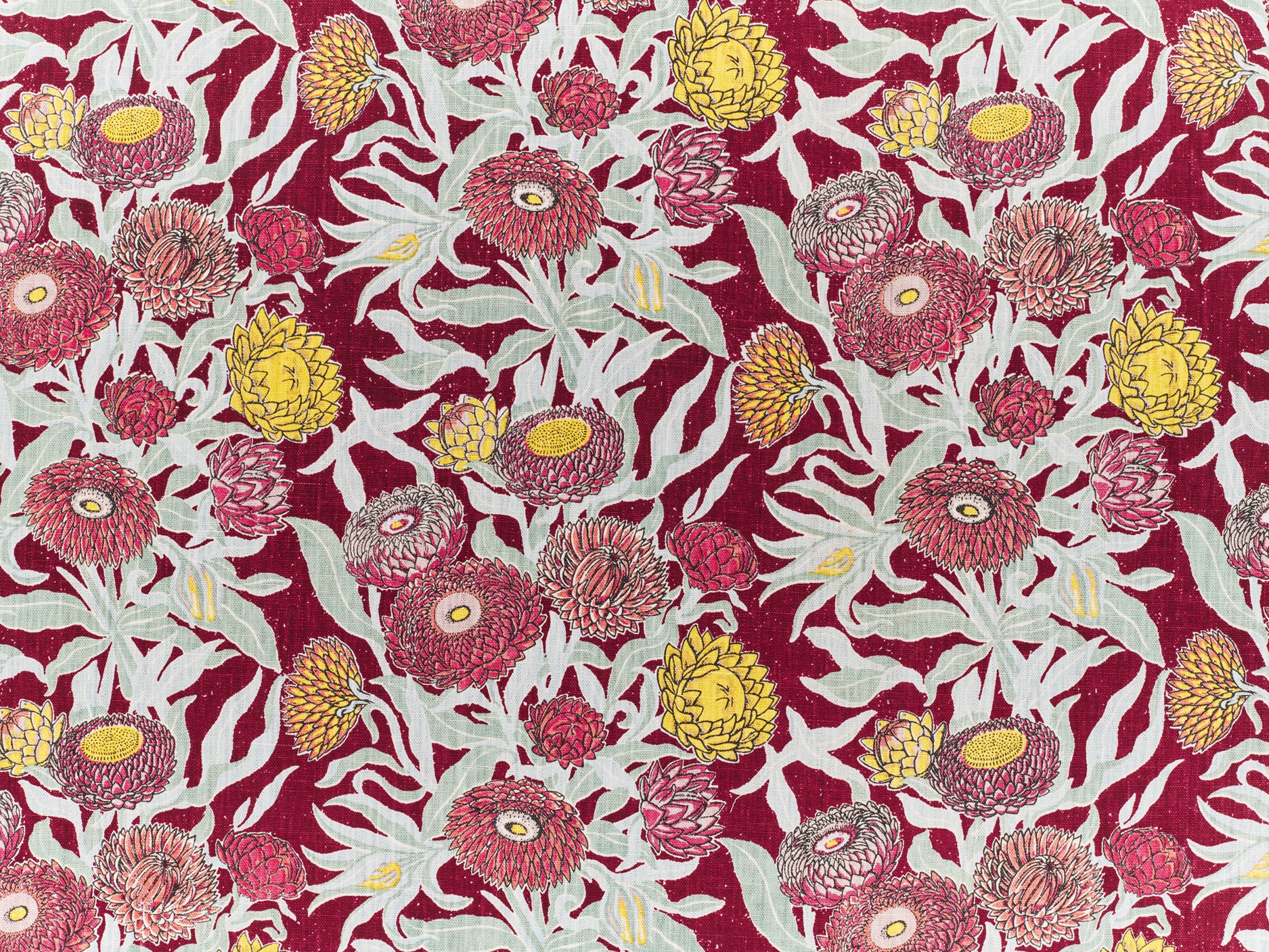 Printed linen in a hand drawn daisy design in shades of red, pink and yellow with sage leaves on a crimson field.