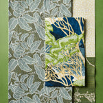 Flatlay with fabric swatches with botanical and leaf patterns in shades of blue, green, beige, and white, arranged on a solid green background.