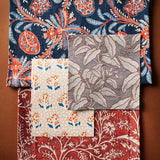 A flat lay with fabric and wallpaper swatches in botanical patterns in a color palette of blue, rust, red, and cream on a warm brown background. 