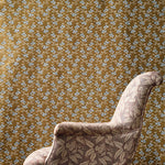 An upholstered armchair with a leafy floral pattern in beige and brown, set against a brown and grey small scale geo-floral fabric backdrop.