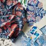 A styled flat-lay of patterned fabric and hand drawn illustrations featuring intricate botanical and floral designs in navy blue, coral red.