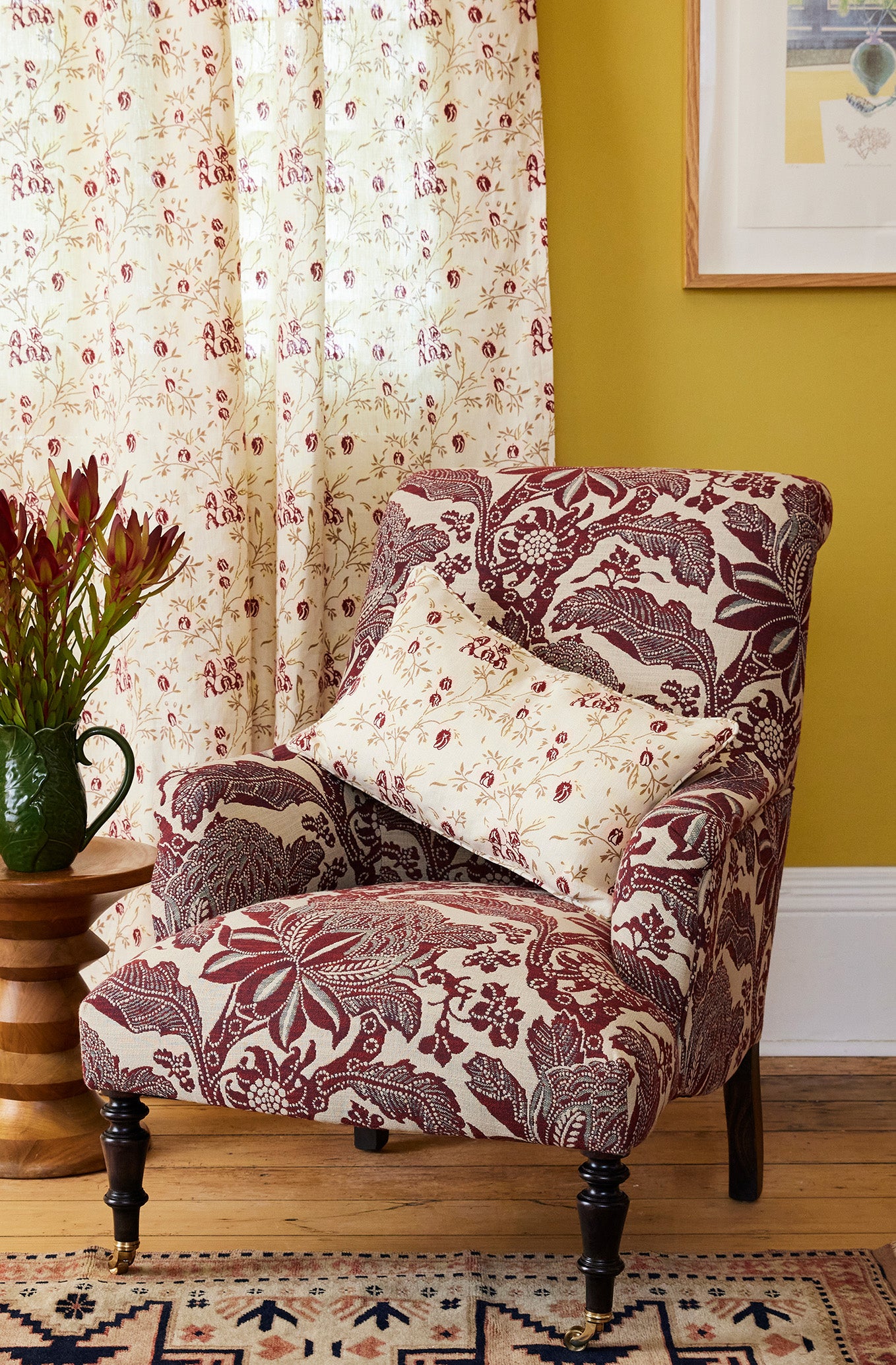 Floral-patterned armchair with a pillow against a yellow wall with a framed picture.
