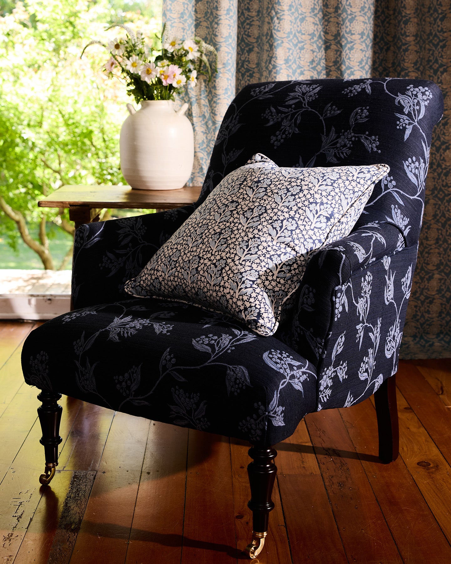 Navy floral armchair with a patterned pillow in a room with a window and curtains.