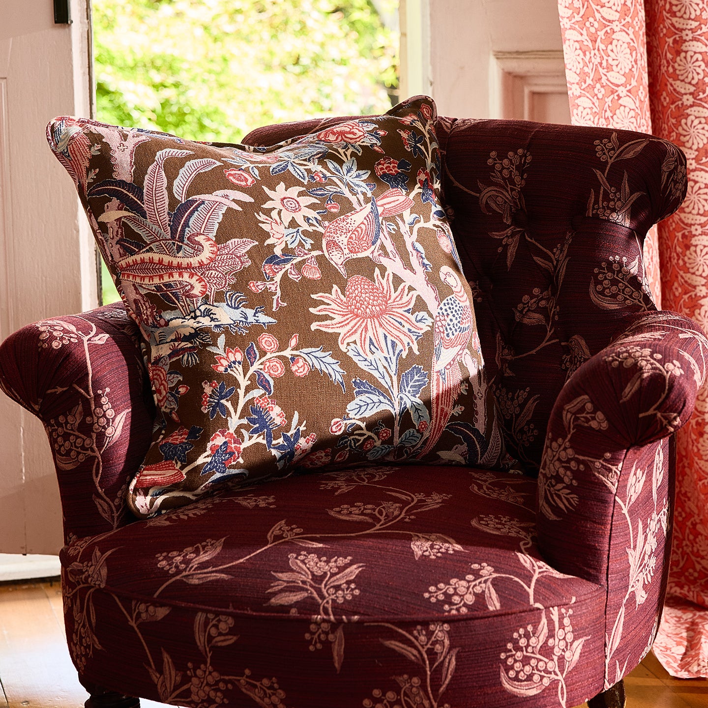 Patterned armchair with a floral pillow in a room with a window and curtains.