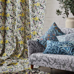 Vignette of a draped bird printed fabrc, with a grey floral patterned couch with a pile of botanical printed pillows. 