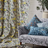 Vignette of a draped bird printed fabrc, with a grey floral patterned couch with a pile of botanical printed pillows. 
