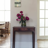 Floral arrangement in a vase on a wooden side table in a room with large windows.