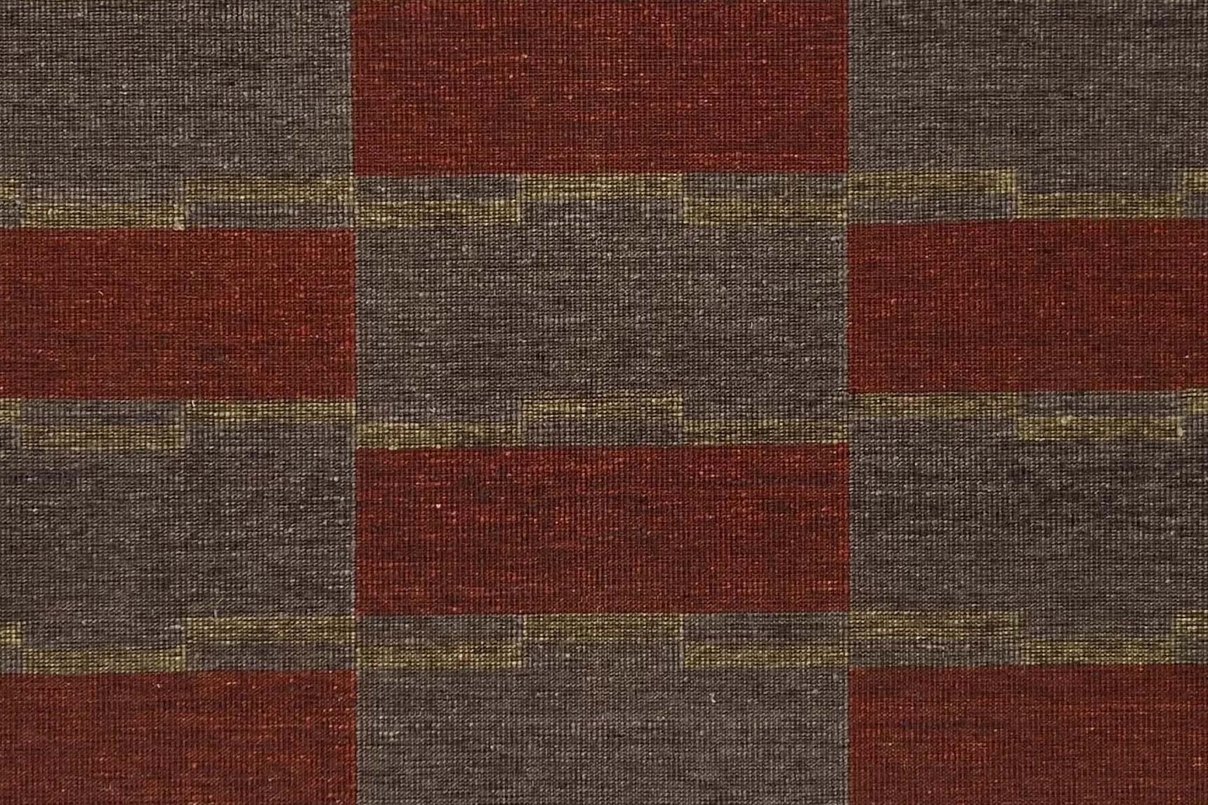 Detail of a handwoven carpet in a geometric design in brown, red with yellow accent. 