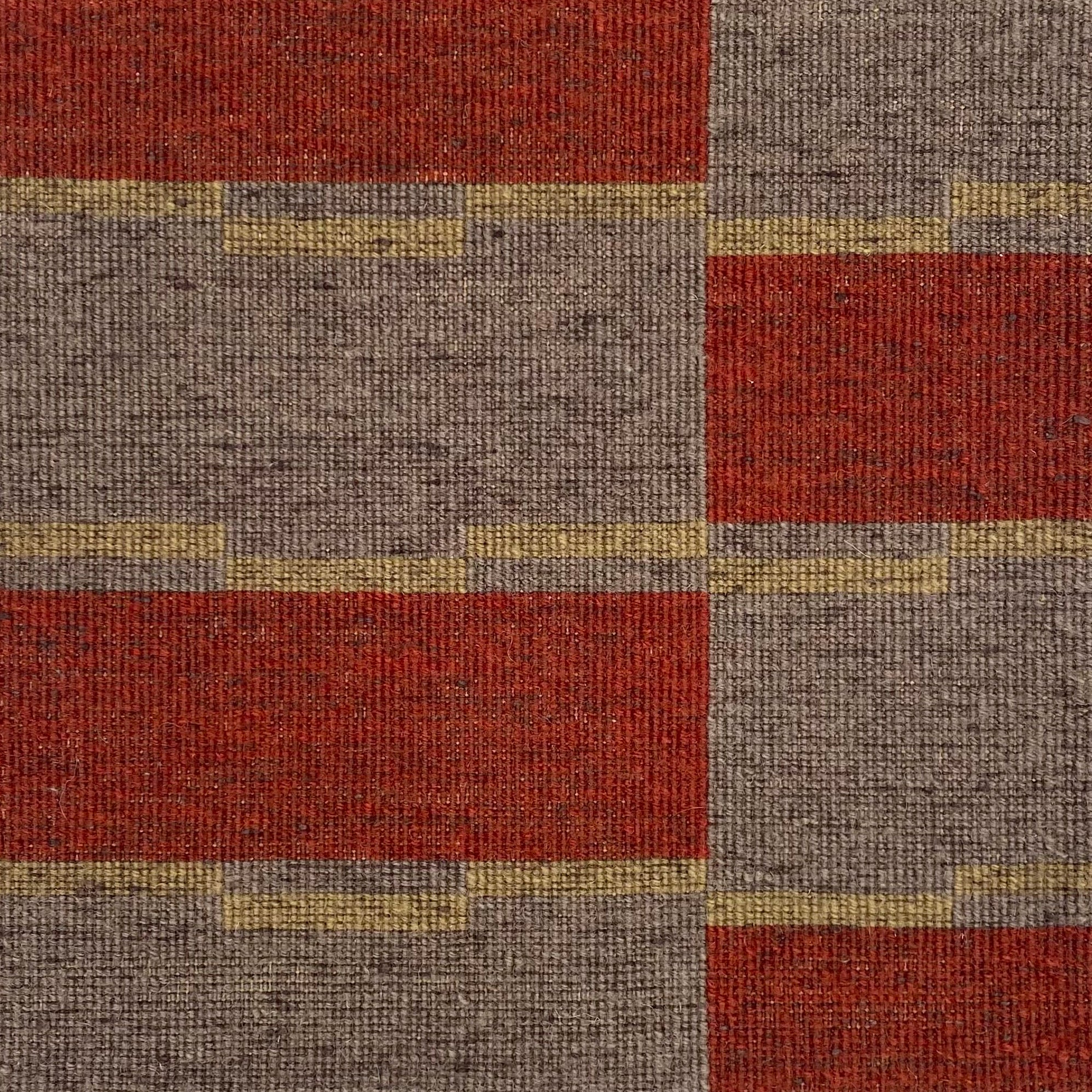 Detail of a handwoven carpet in a geometric design in brown, red with yellow accent. 
