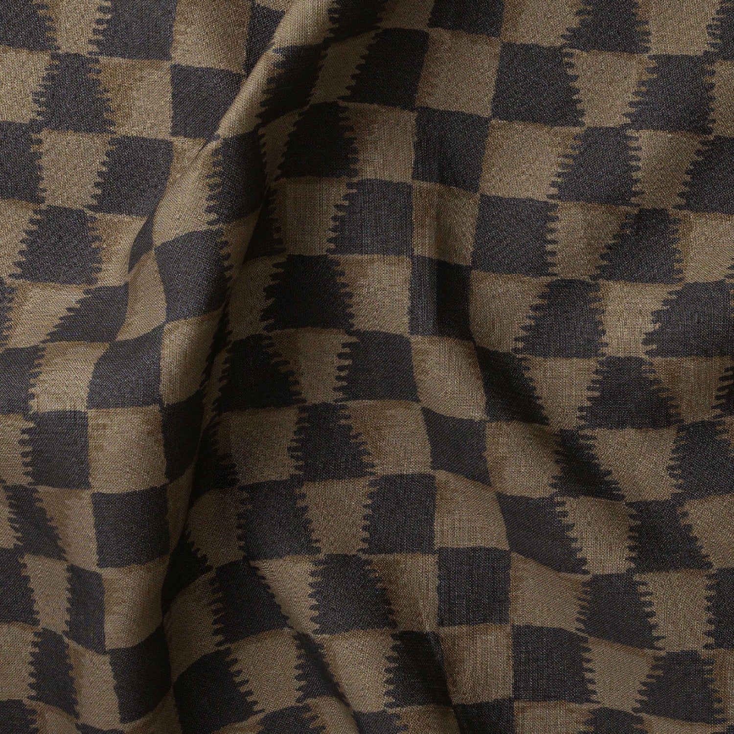 Detail of gently draped printed fabric in a watercolor ikat-inspired checkerboard pattern in muted black and warm tan.