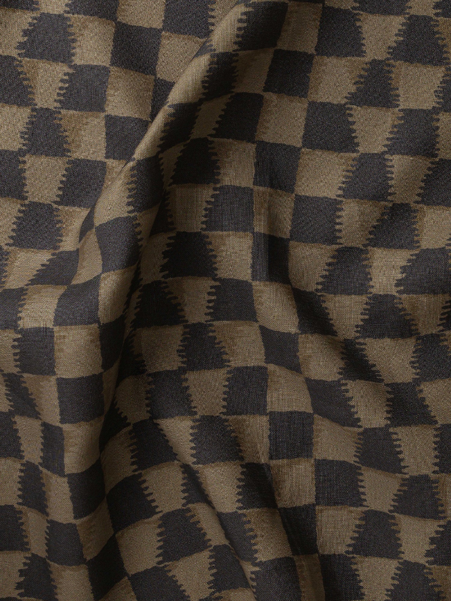 Detail of gently draped printed fabric in a watercolor ikat-inspired checkerboard pattern in muted black and warm tan.