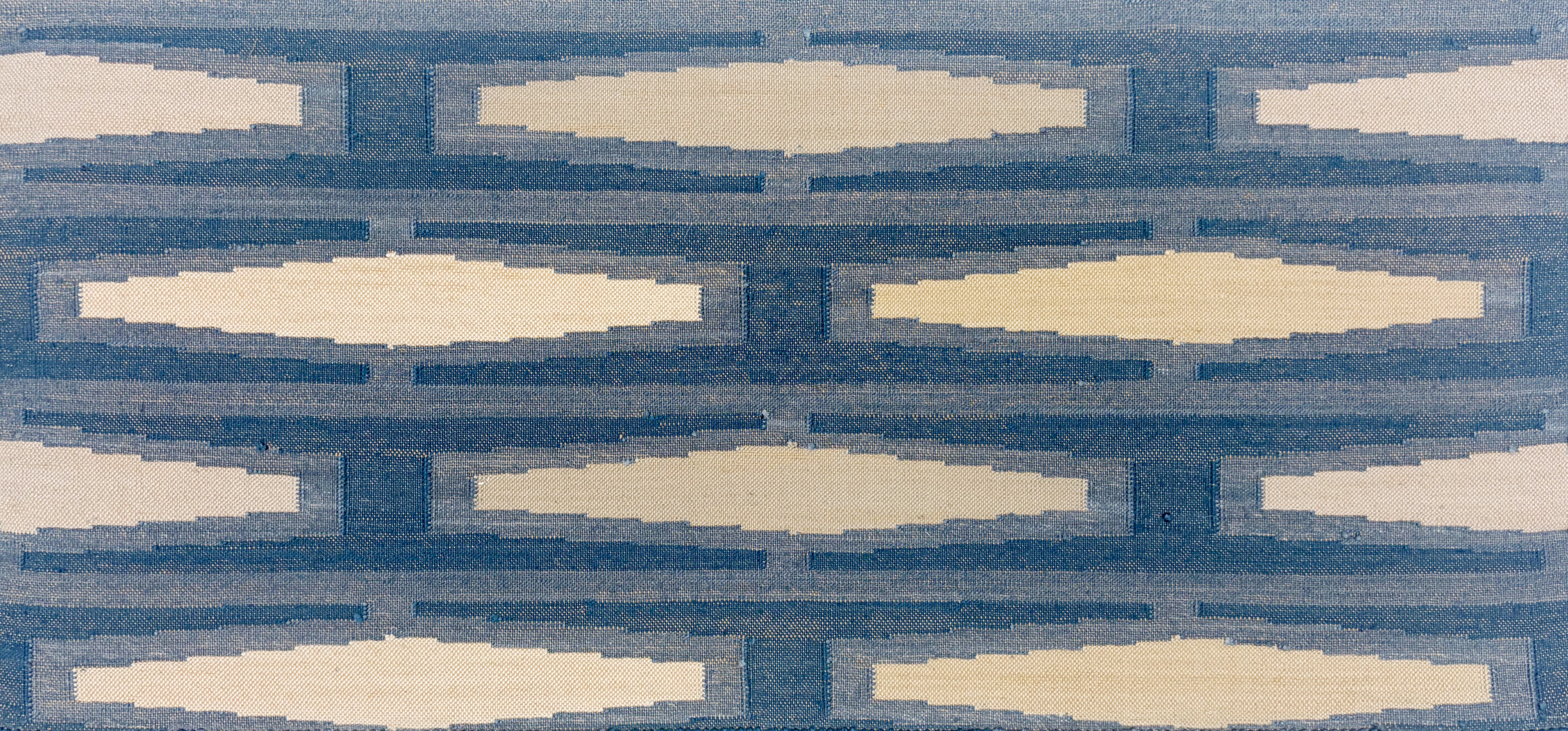 Close up of a handmade flatweave rug with a geometric tiled design in cream and shades of blue. 