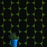 A vase of flowers stands in front of a wall papered in an abstract curvilinear pattern in gray on an olive field.