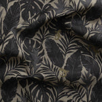 Detail of gently draped printed fabric in a tropical palm frond pattern in faded black and charcoal grey scattered with small tan lizards. 