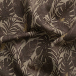 Detail of gently draped printed fabric in a tropical palm frond pattern in tonal brown scattered with small tan lizards. 