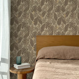 Bed with tan linens and wooden headboard, wooden side table  with white book and green glass, white floor length curtain against a taupe tropical palm frond wallpaper. 