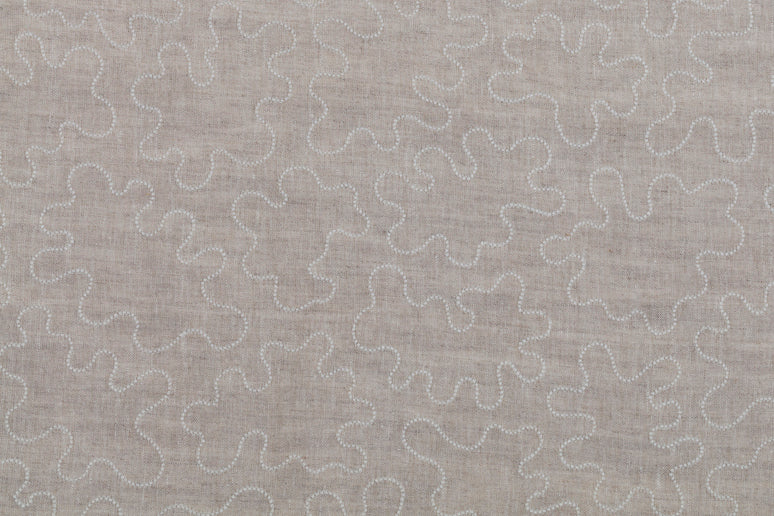 Detail of fabric with an abstract embroidered pattern in white on a cream field.