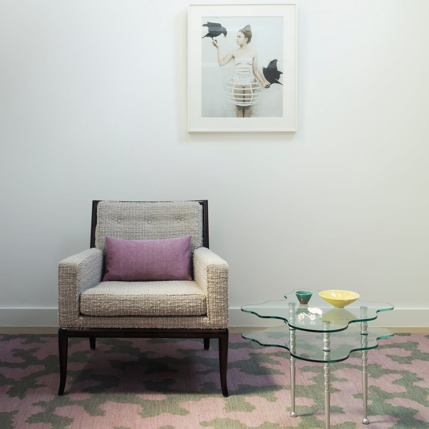 Side chair in white bouclé against a wall with atop a andwoven rug in an abstract coral design grey and purple with a tan accent line, with an organic cloud shaped side table with orange metal legs. 