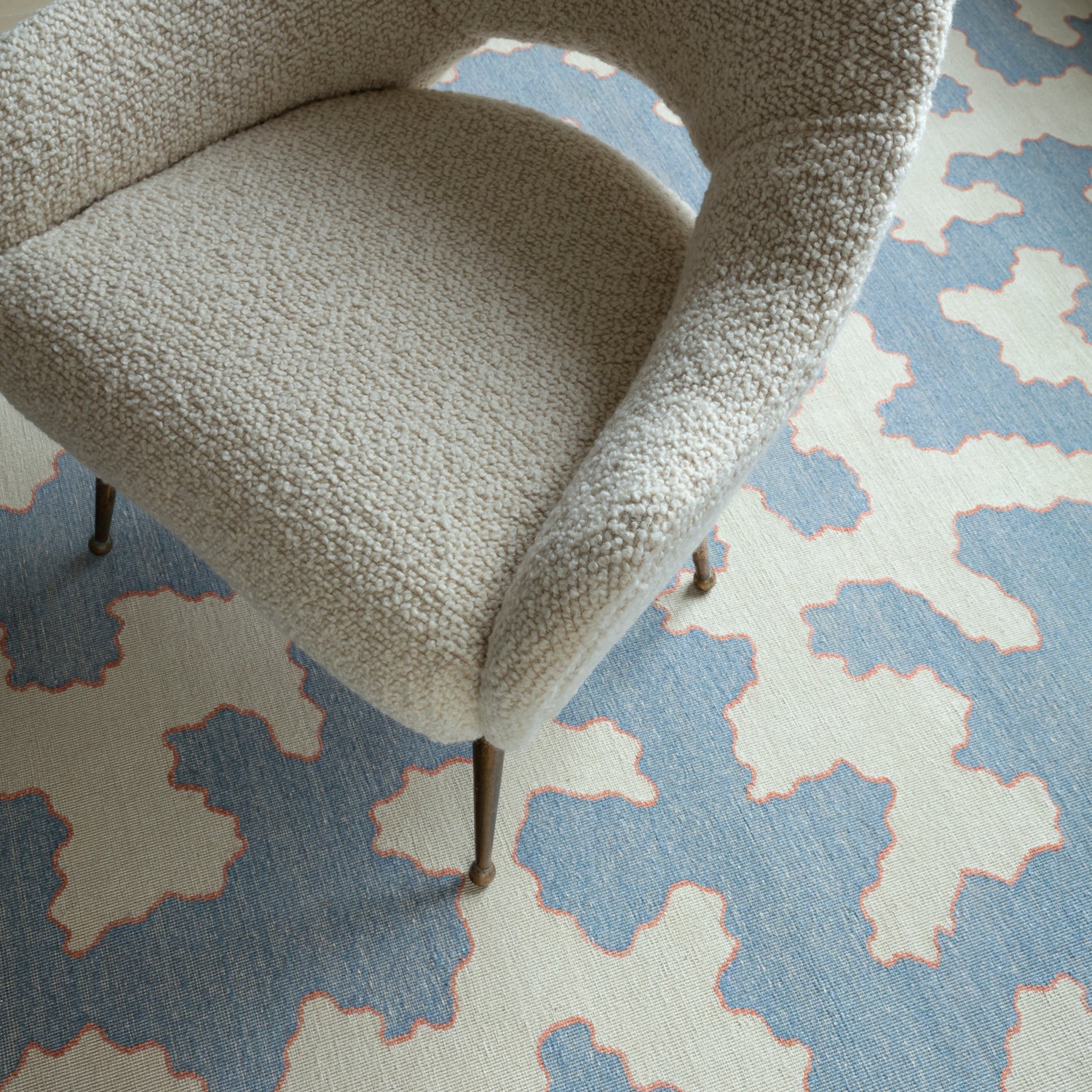 Side chair in a white bouclé on top of a handwoven rug in an abstract coral design in blue and white with a red accent.