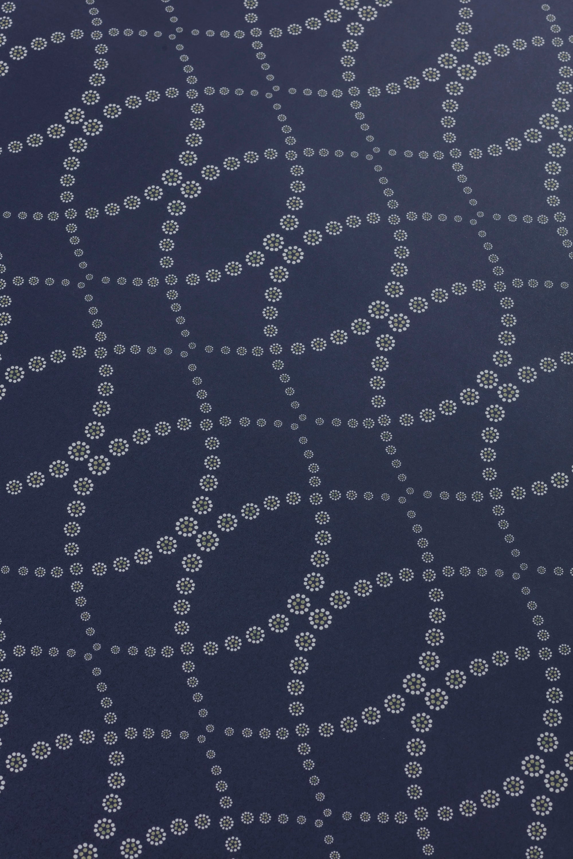 Detail of a wallpaper in a playful floral lattice print in white and tan on a navy blue field.
