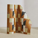 A curved partition stands on the ground, covered in a geometric grid print in rust, yellow, gray and cream.