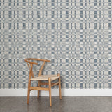Angled wooden chair with woven seat on concrete floor against wallpaper in a large-scale checked pattern in shades of steel blue and pale grey.