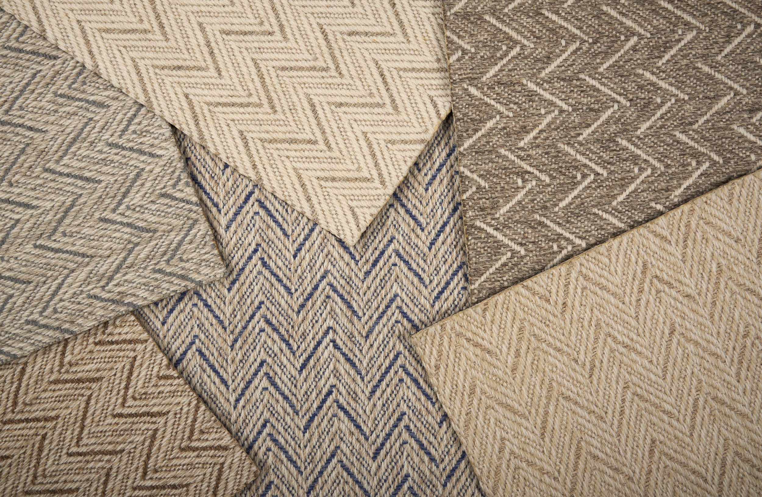 Stack of broadloom carpet samples in a herringbone pattern in array of neutral colors.