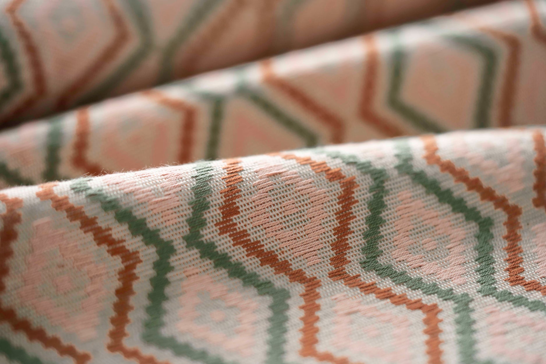Close-up of patterned fabric with geometric design in brown, pink, and green.