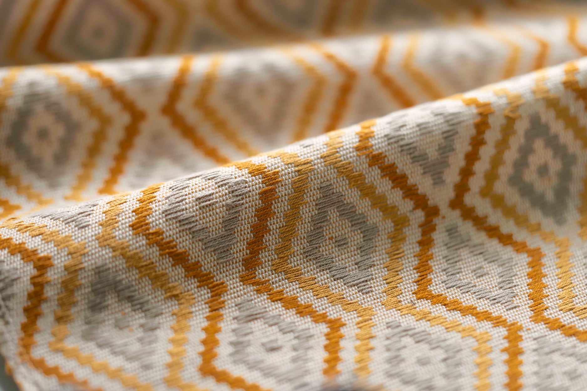 Close-up of fabric with a geometric pattern in yellow beige, and white.