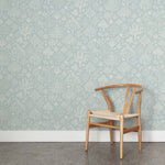A wooden chair stands in front of a wall papered in a playful animal and tree print in white on a light blue field.