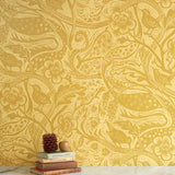 A stack of books stands in front of a wall papered in a playful wren and flower print in yellow and gold.