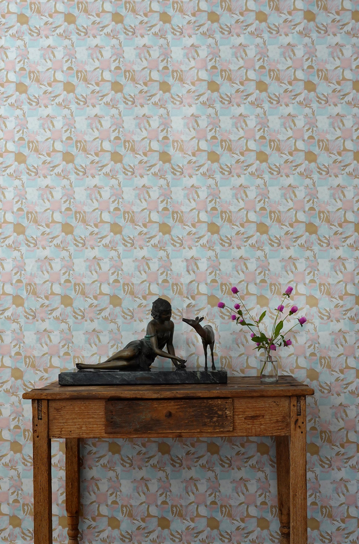 Wooden table with decorative items against a blue and ink tropical check patterned wallpaper.