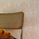 Chair with woven backrest against a tropical checkerboard patterned wall in pinky orange. 