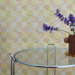 Glass table with a vase of purple flowers against a yellow tropical checkerboard patterned wall.