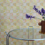Glass table with a vase of purple flowers against a yellow tropical checkerboard patterned wall.