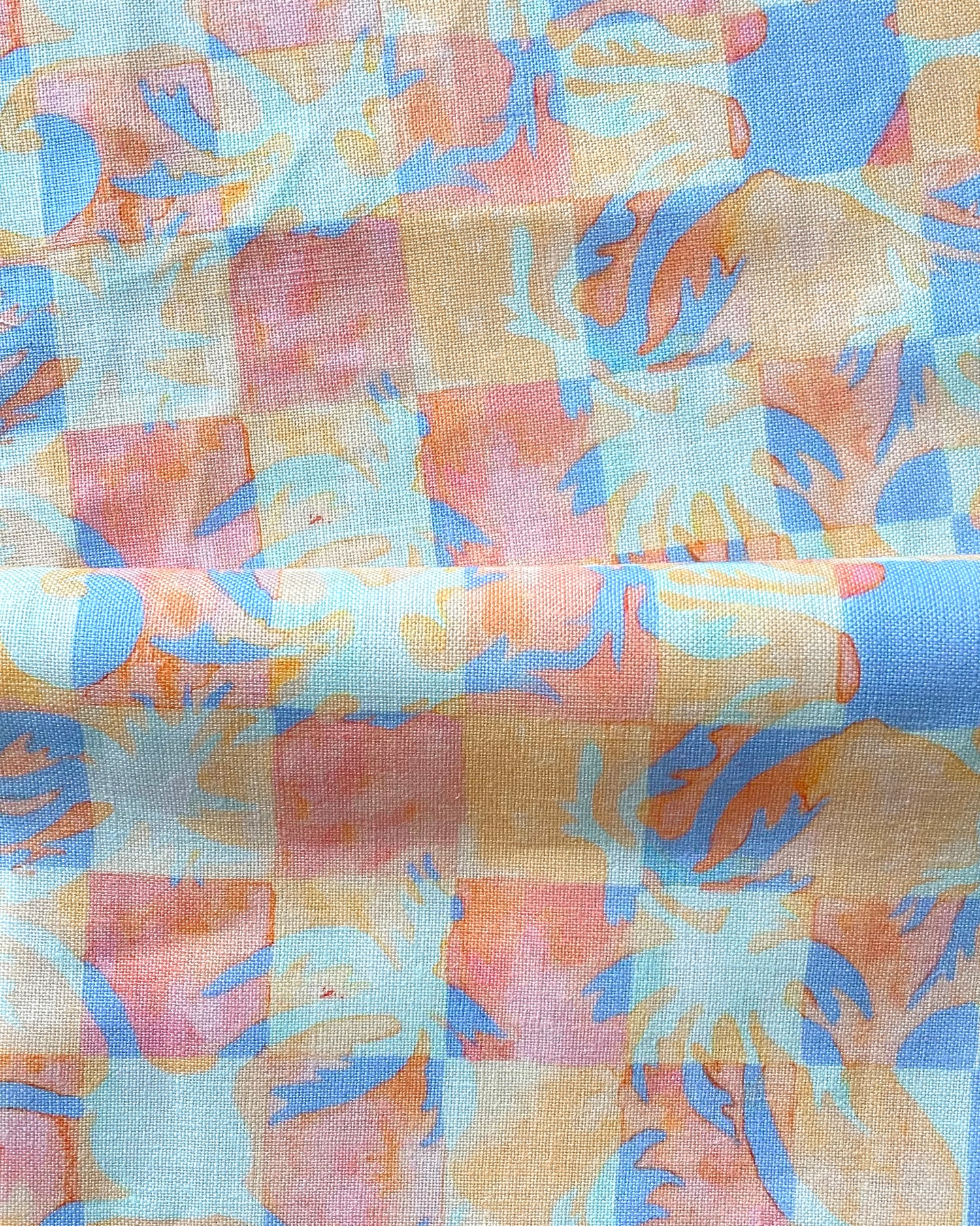 Draped fabric in a painterly tropical checkerboard design in blue, coral and orange. 