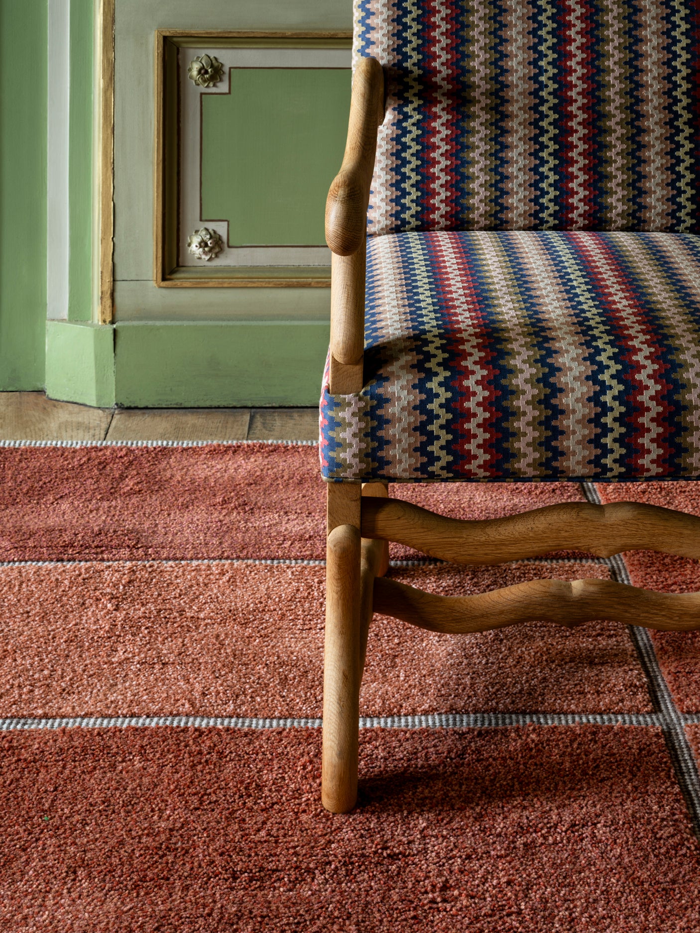Chair with patterned fabric on a red carpet in a room with green walls.