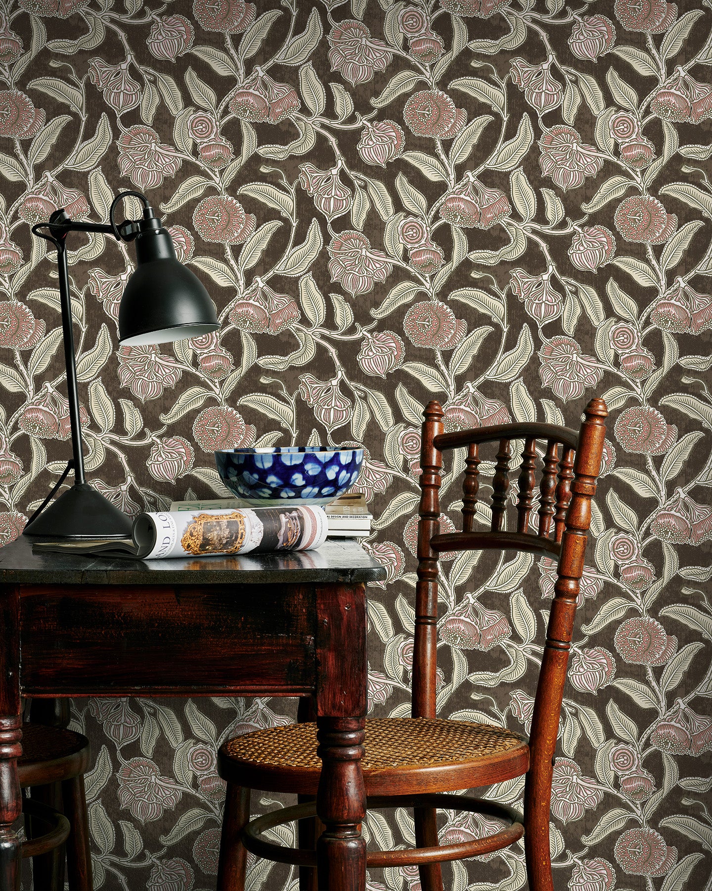 Room interior with a wooden table, chair, and lamp against a brown and pink floral-patterned wall.
