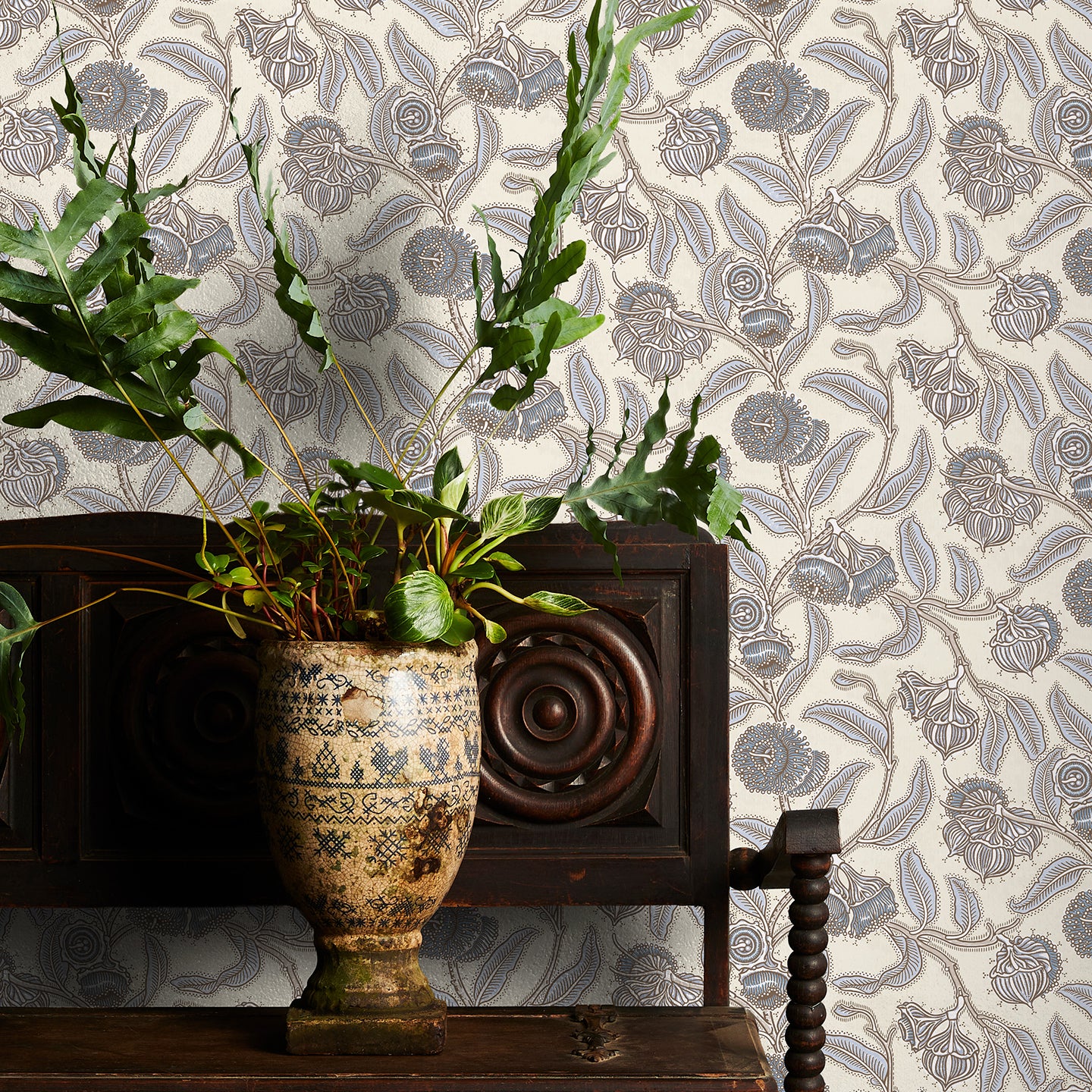 Decorative wallpaper with cream and blue floral pattern, plant in vase on wooden cabinet
