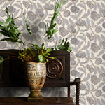 Decorative wallpaper with cream and blue floral pattern, plant in vase on wooden cabinet