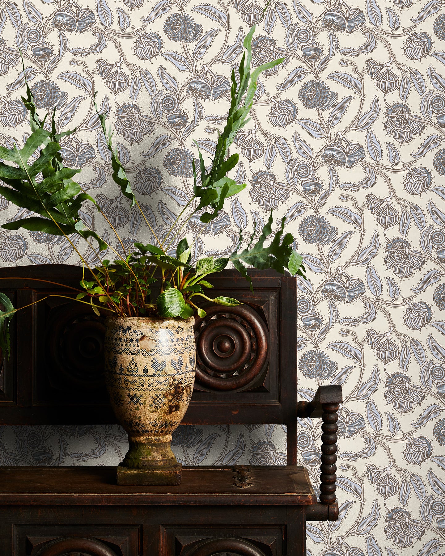 Decorative wallpaper with cream and blue floral pattern, plant in vase on wooden cabinet