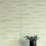A vase of flowers stands in front of a wall papered in an abstract zigzag pattern in light green on a green field.